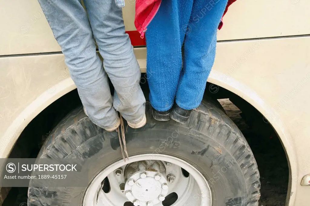 Two children standing on car tire, Lima, Peru