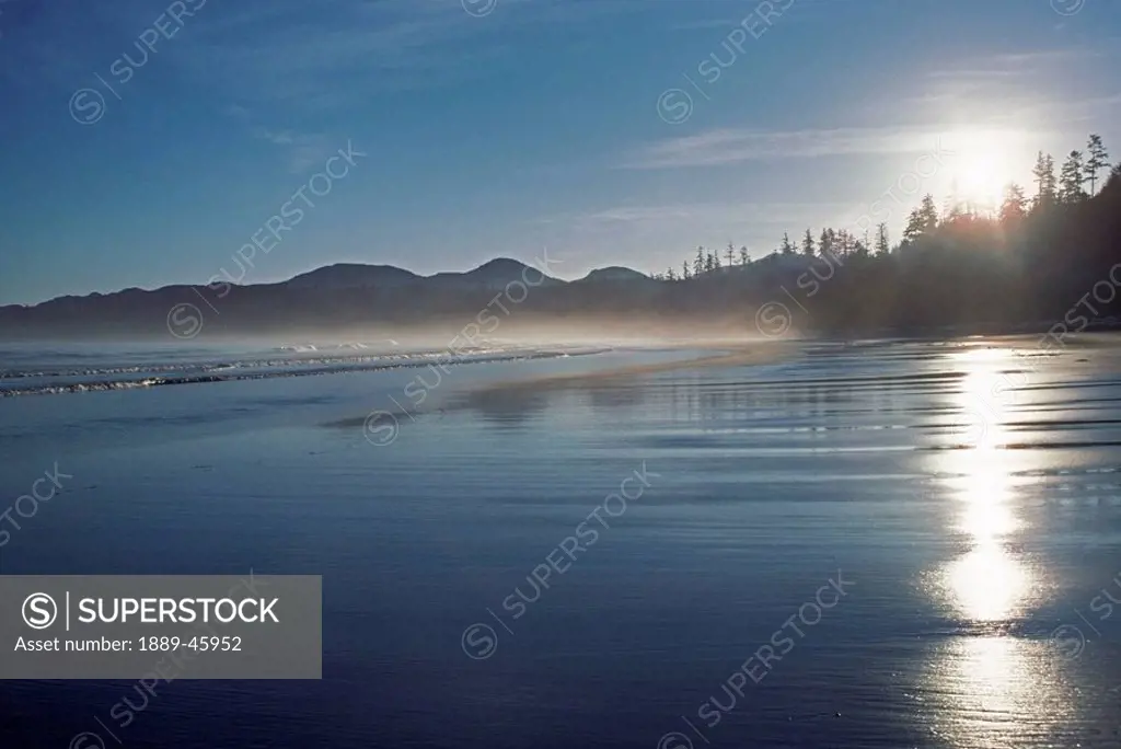the setting sun shines on the wet beach as the waves roll in to shore