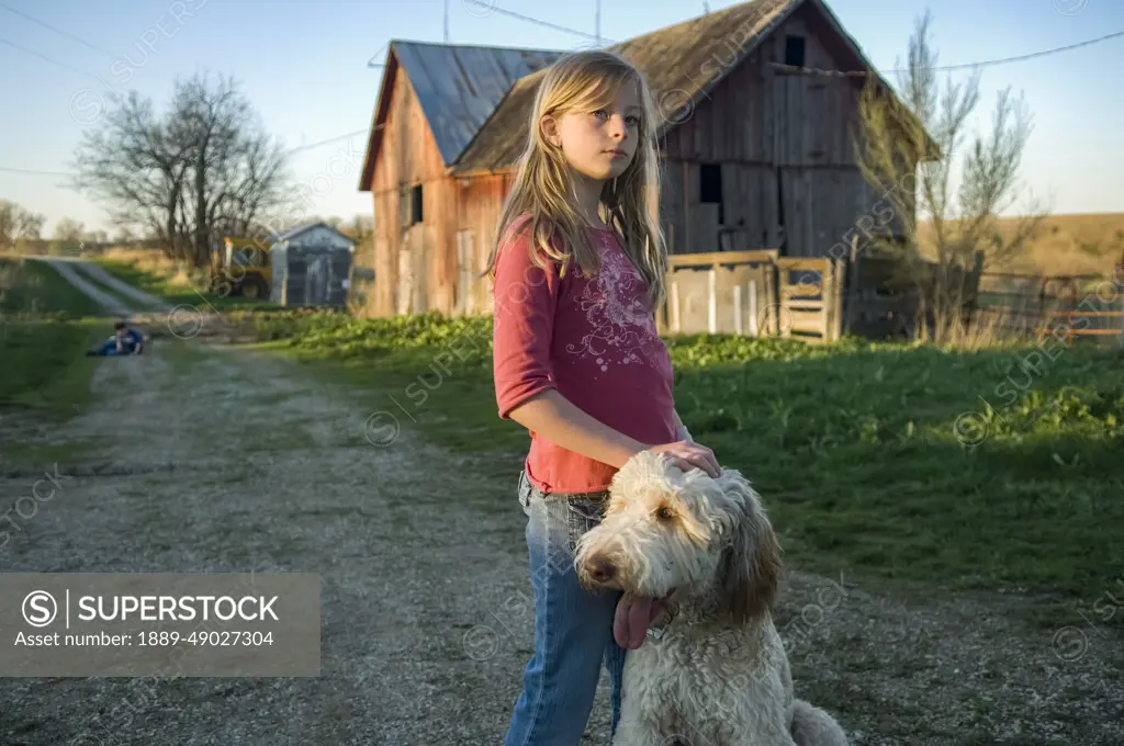 Girl stands near a barn with her pet dog; Dunbar, Nebraska, United States of America