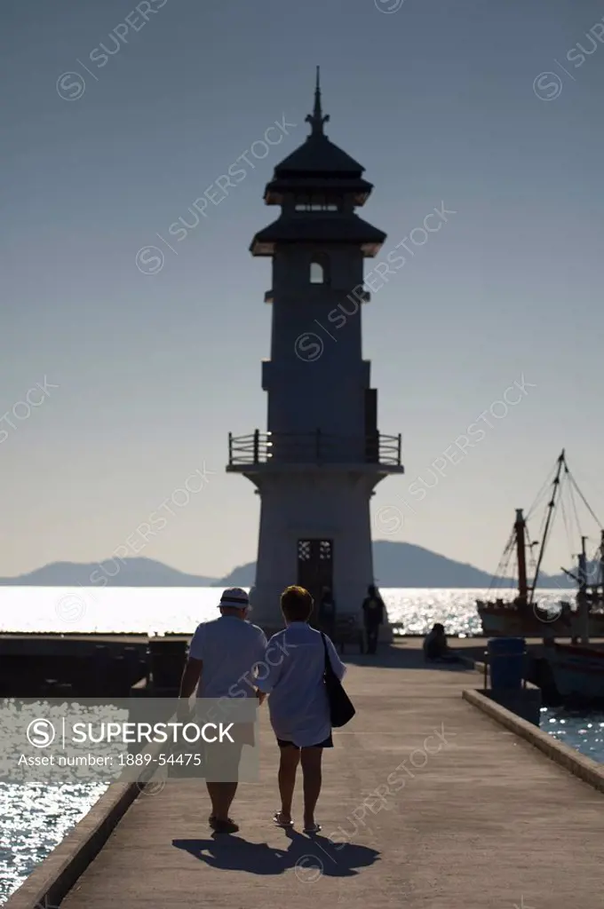 Thailand, People Walking Out On A Pier Towards A Lighthouse