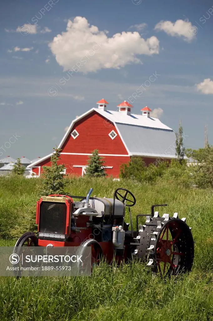 old red tractor in a field with a red barn in the background, alberta, canada