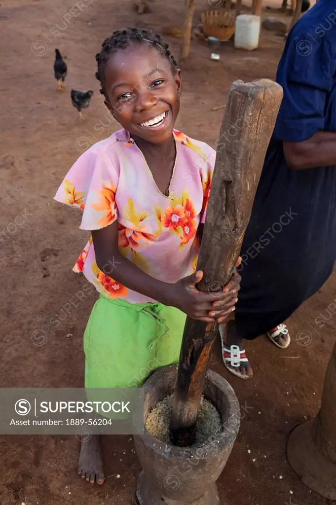 a girl pounding corn into flour by hand, manica, mozambique, africa