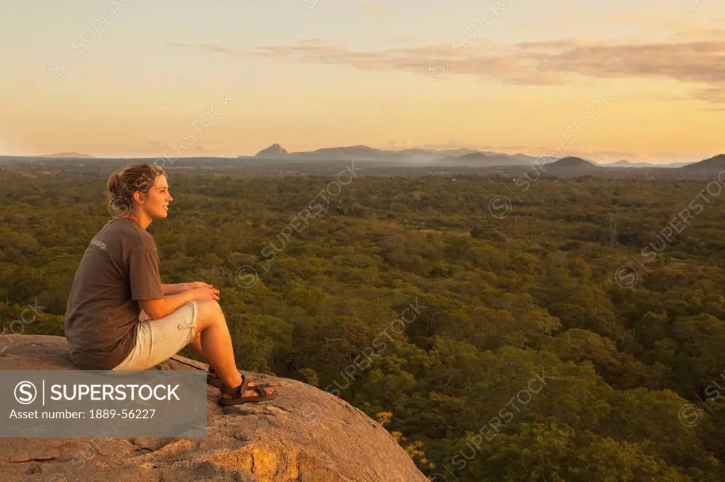 a young woman sits on a rock and looks out over the landscape, manica, mozambique, africa