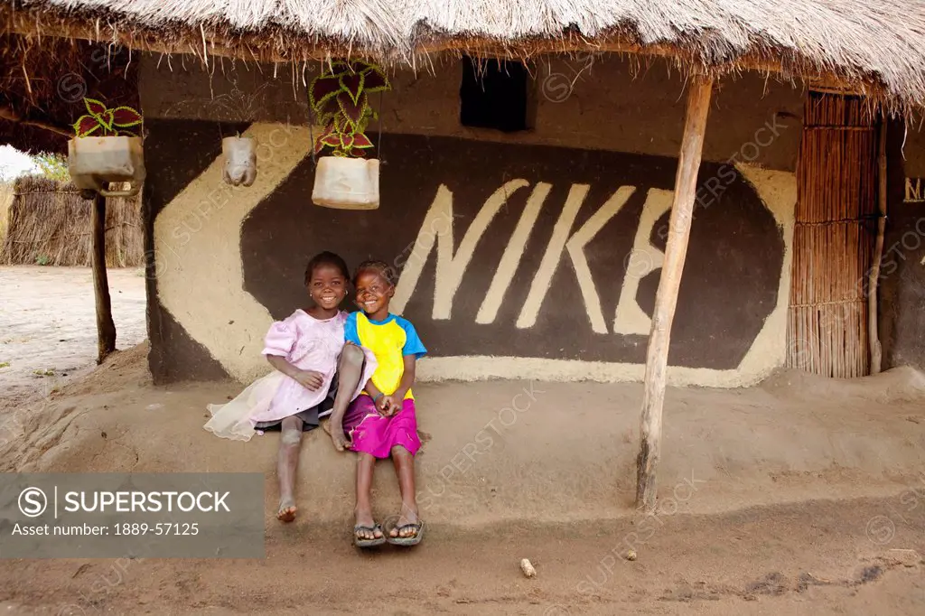 Two Children Sit Beside A Hand Painted Nike Sign, Manica, Mozambique, Africa