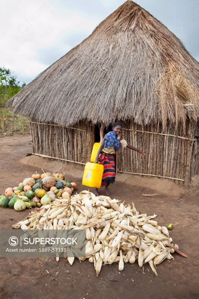 A Young Woman Carries A Heavy Water Jug Past Piles Of Fish And Vegetables On The Ground, Manica, Mozambique, Africa