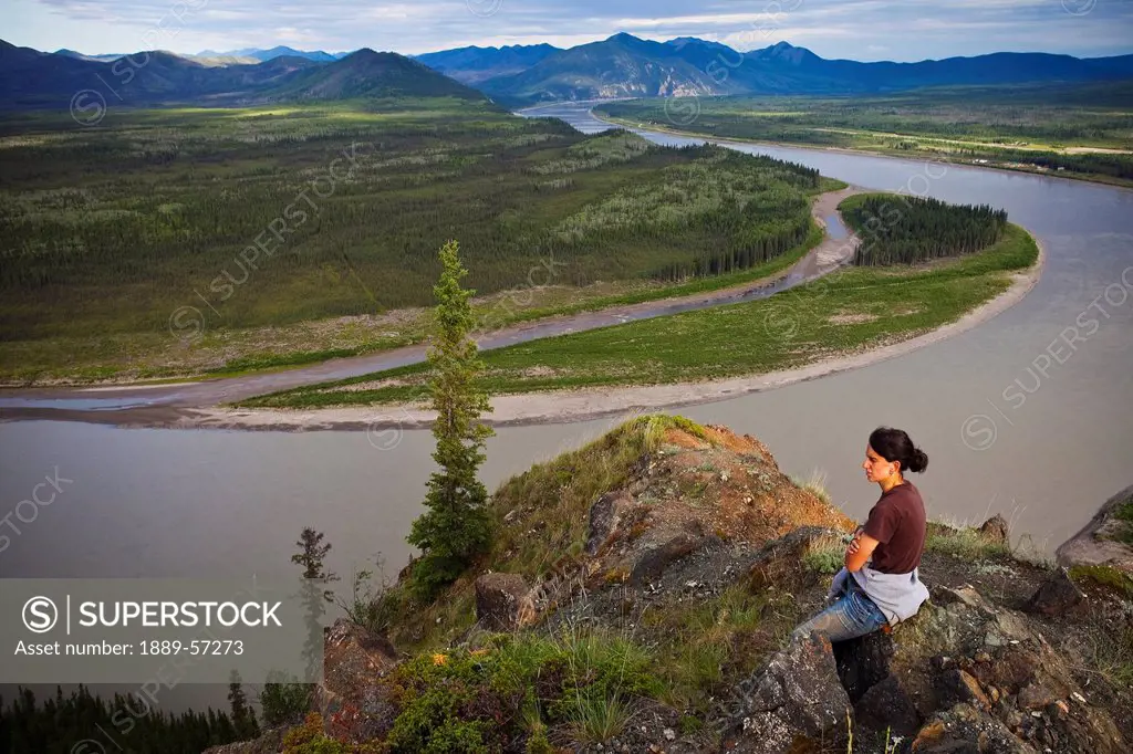 A Woman Sits On A Rock Enjoying A View Of The Yukon River, Eagle, Alaska, United States Of America