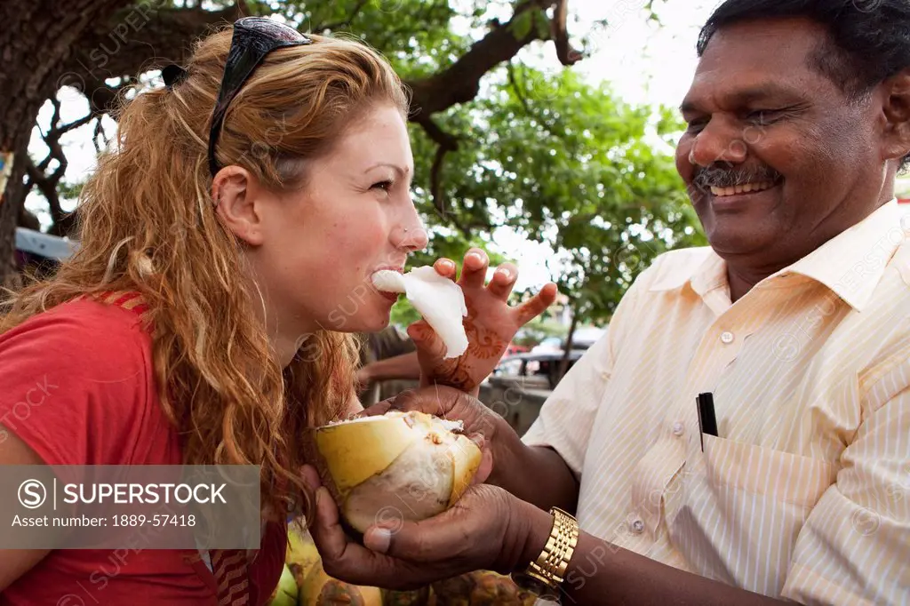 a woman eating the flesh of a coconut when offered to her by a man, mysore, karnataka, india