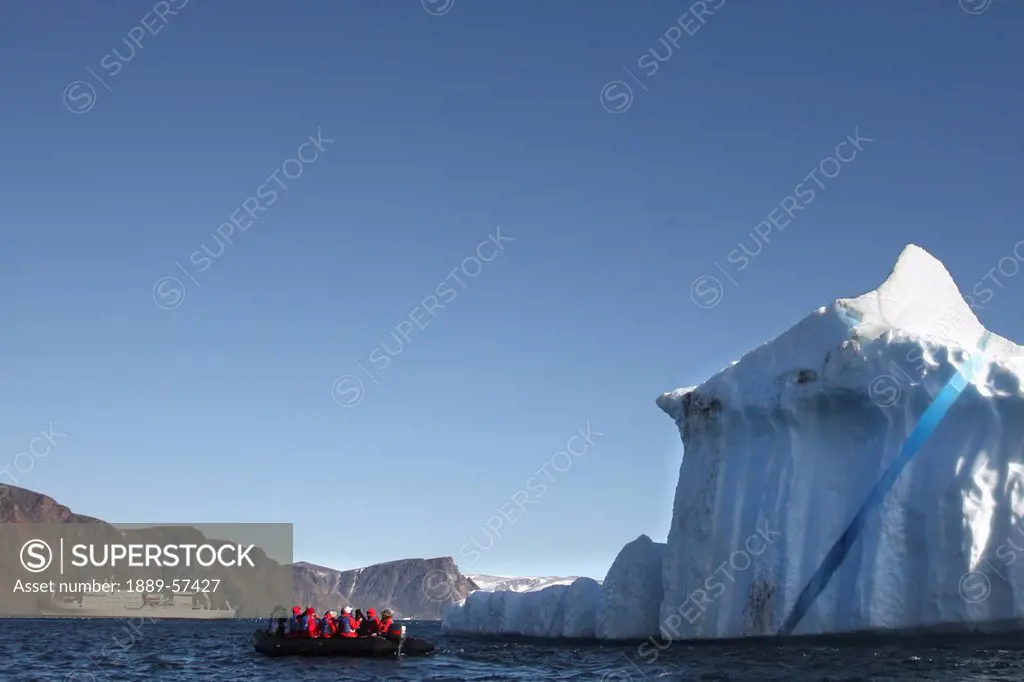 iceberg and tourists on an inflatable raft with their boat in the background, devon island, nunavut, canada