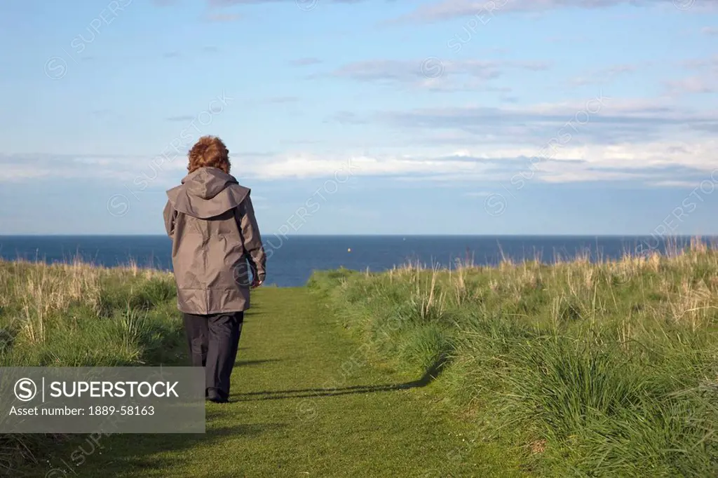 Woman walking path to seashore, South Shields, Tyne and Wear, England
