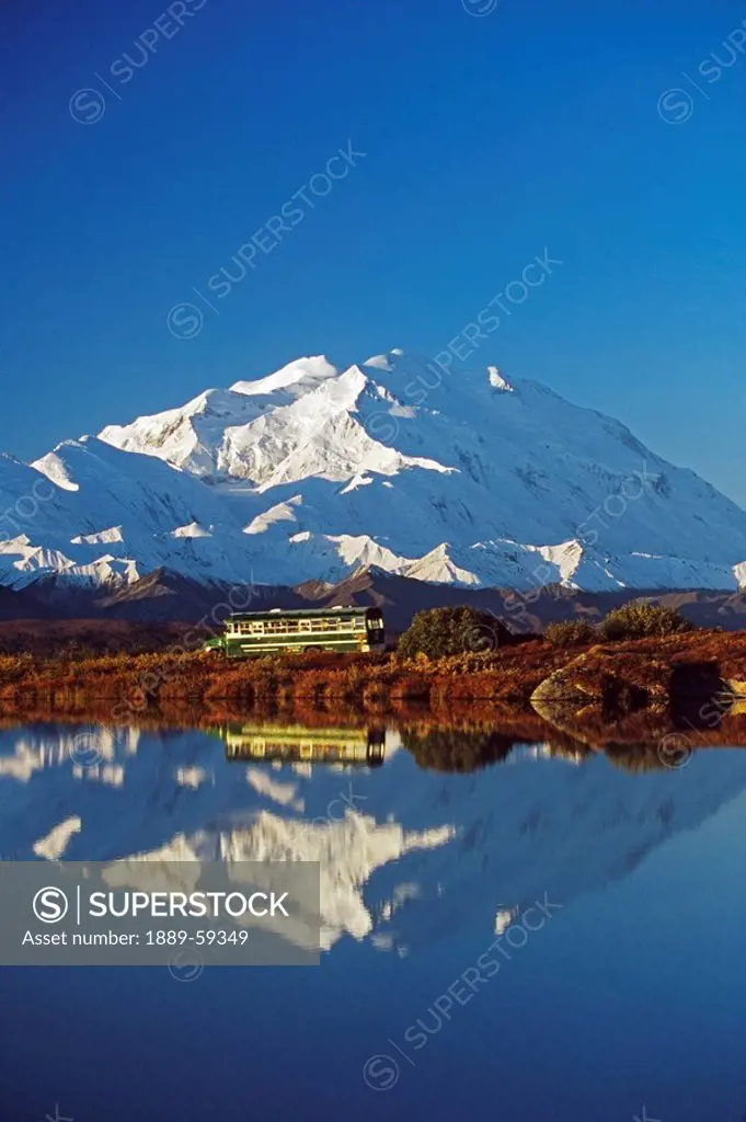 Visitor bus passes along tundra pond with reflection of Mount McKinley, Alaska