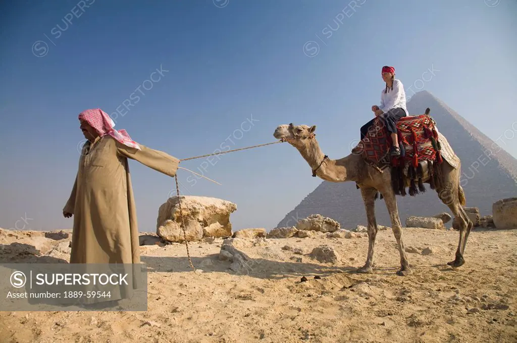 Young woman tourist on a camel being led by a guide at the Pyramids of Giza, Cairo, Egypt