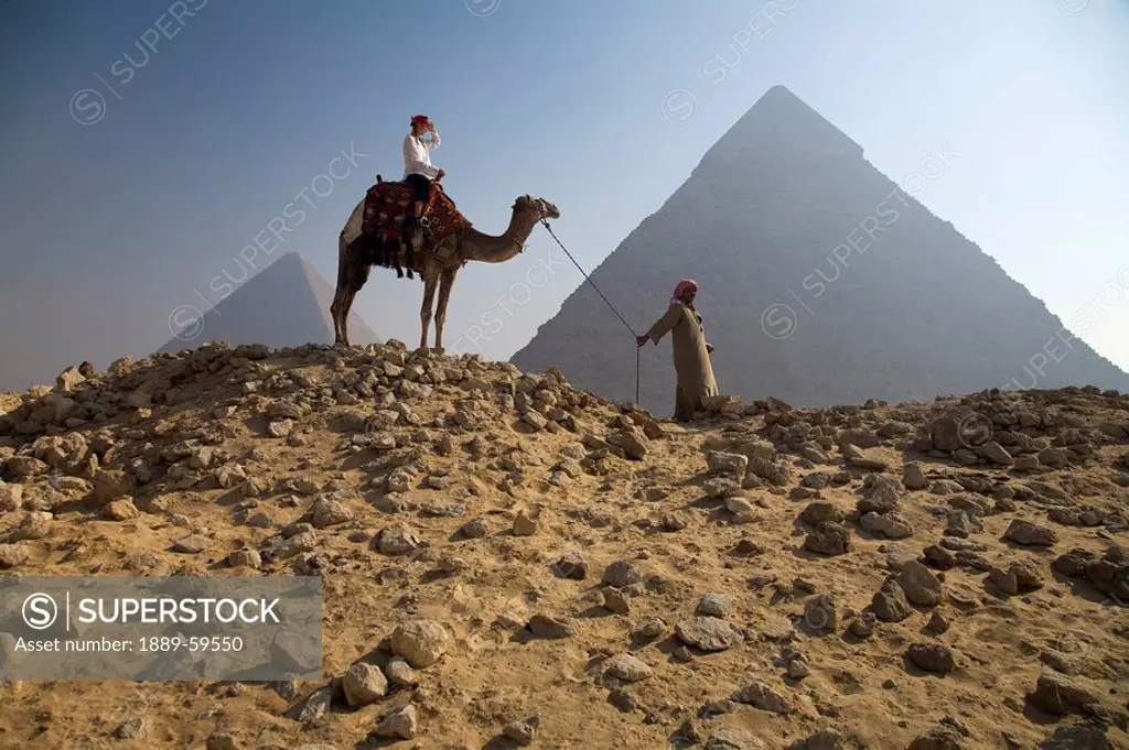 Young woman tourist on a camel led by a guide at the Pyramids of Giza, Egypt