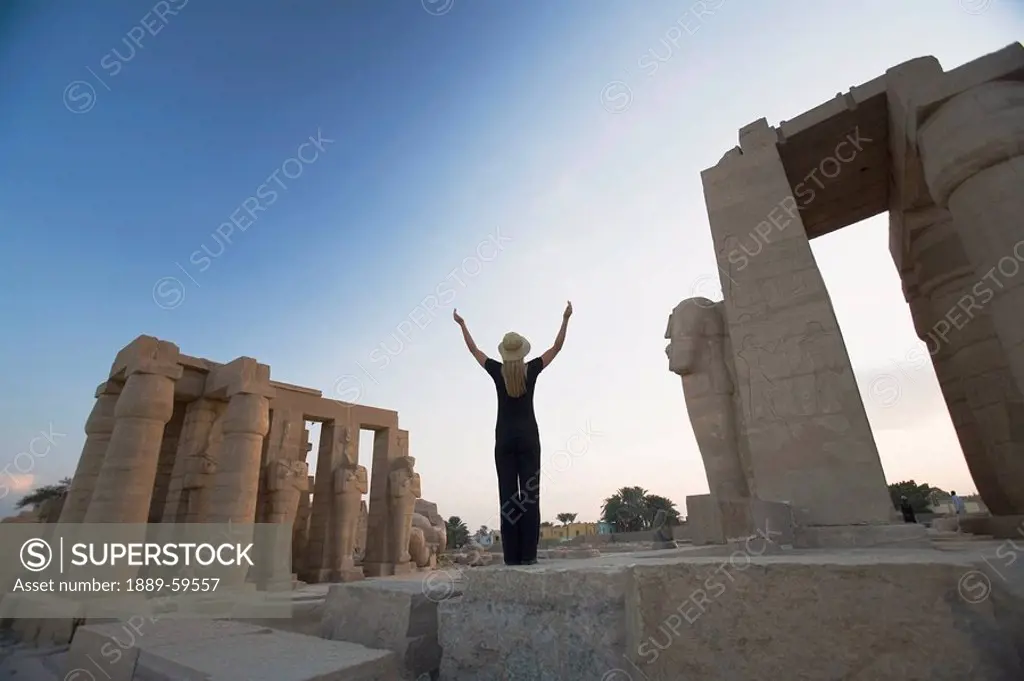 Woman tourist with arms raised at the Ramesseum, Luxor, Nile Valley, Egypt