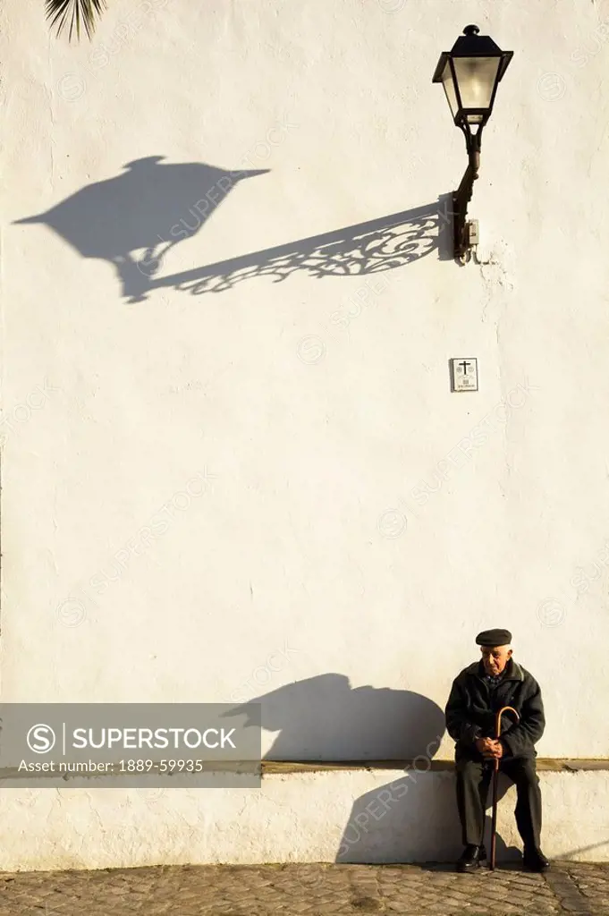 Vejer De La Frontera, Andalusia, Spain, An Elderly Man Sitting Against A White Building