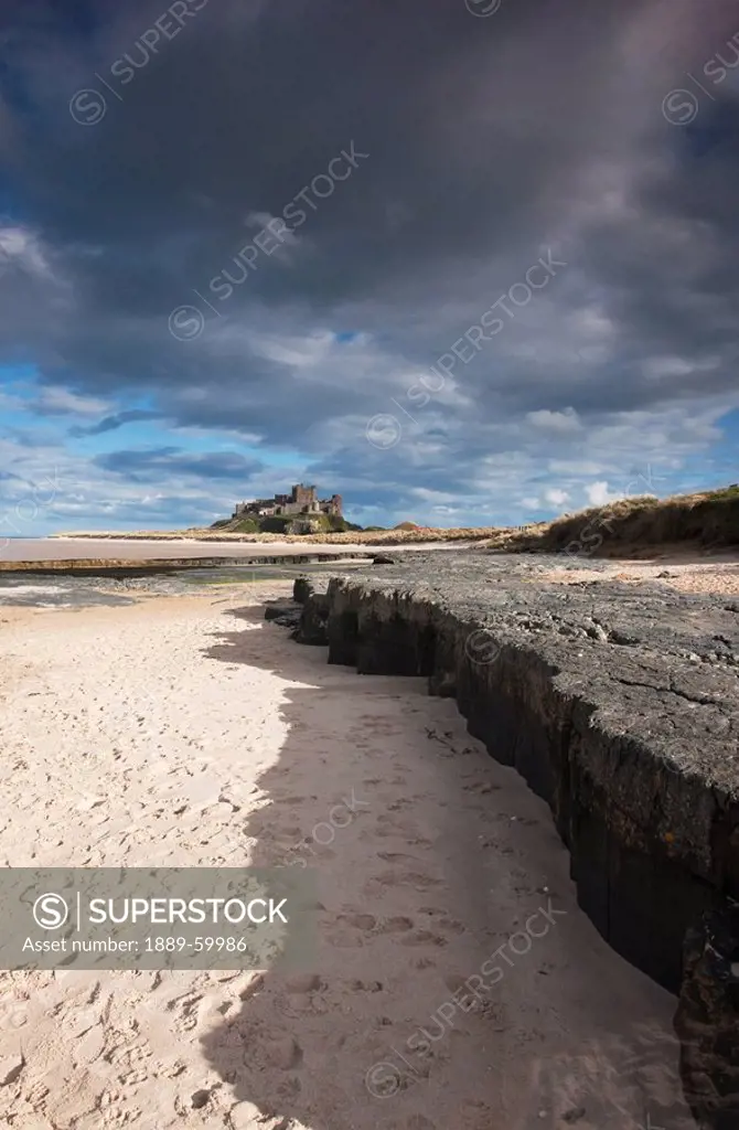 Bamburgh, Northumberland, England, Sand Along A Rock Ledge With Dark Clouds In The Sky