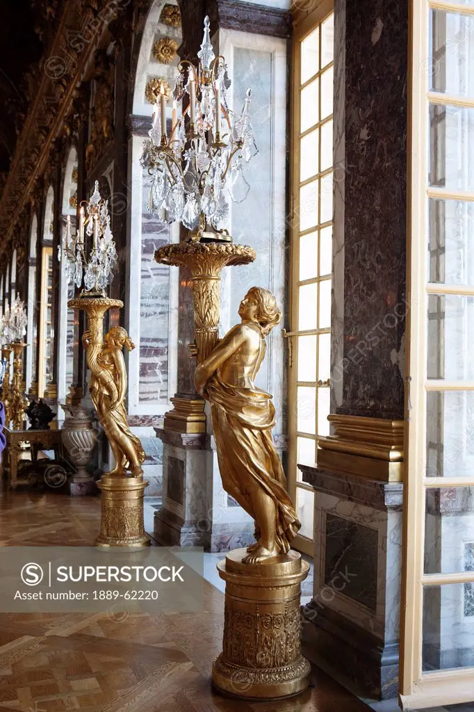 gold statues along the windows holding large glass candle chandeliers, paris, france