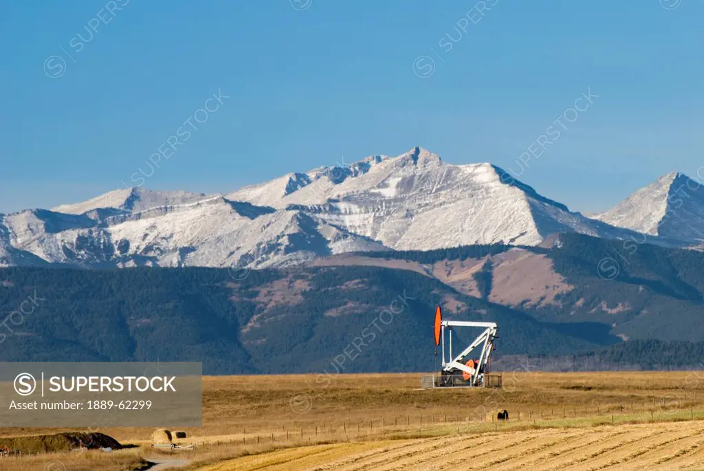 hay bales and an oil pump in a field with mountains in the distance in southern alberta, pincher creek, alberta, canada