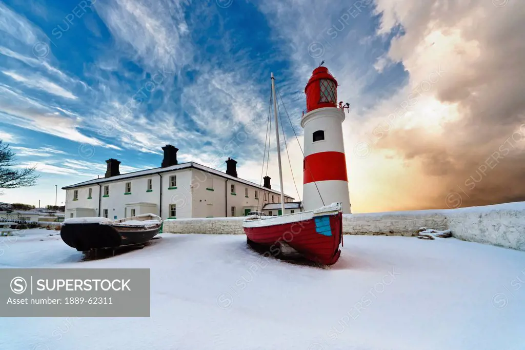 boats sitting on a frozen surface with a lighthouse and building in the background, south shields, tyne and wear, england