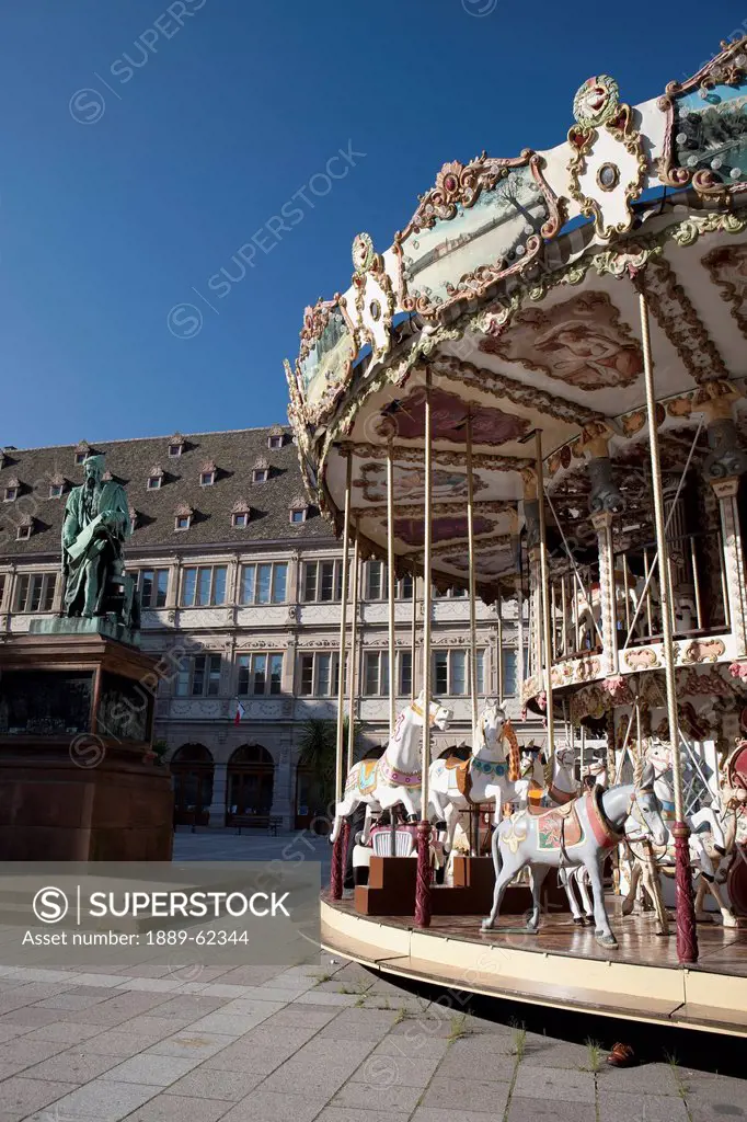 carousel in the town square with a bronze statue and blue sky, strasbourg, france