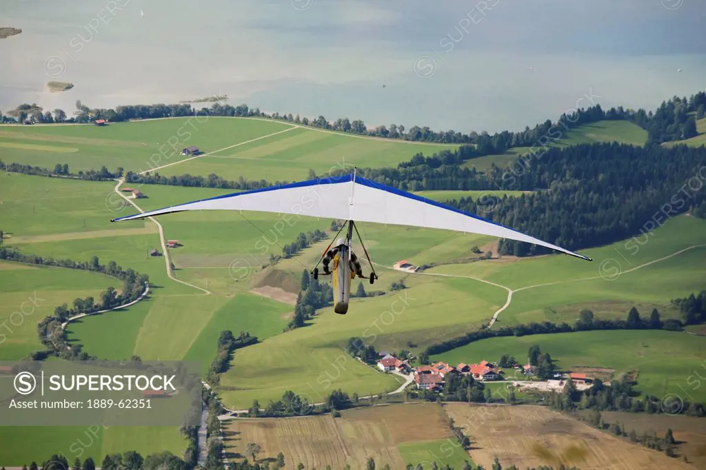 hang glider flying over fields and lake below, schwangau, germany
