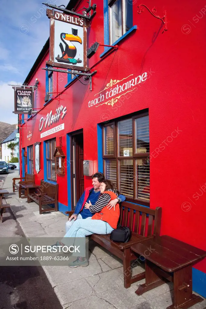 a couple sits on a bench outside o´neill´s pub, allihies, county cork, ireland