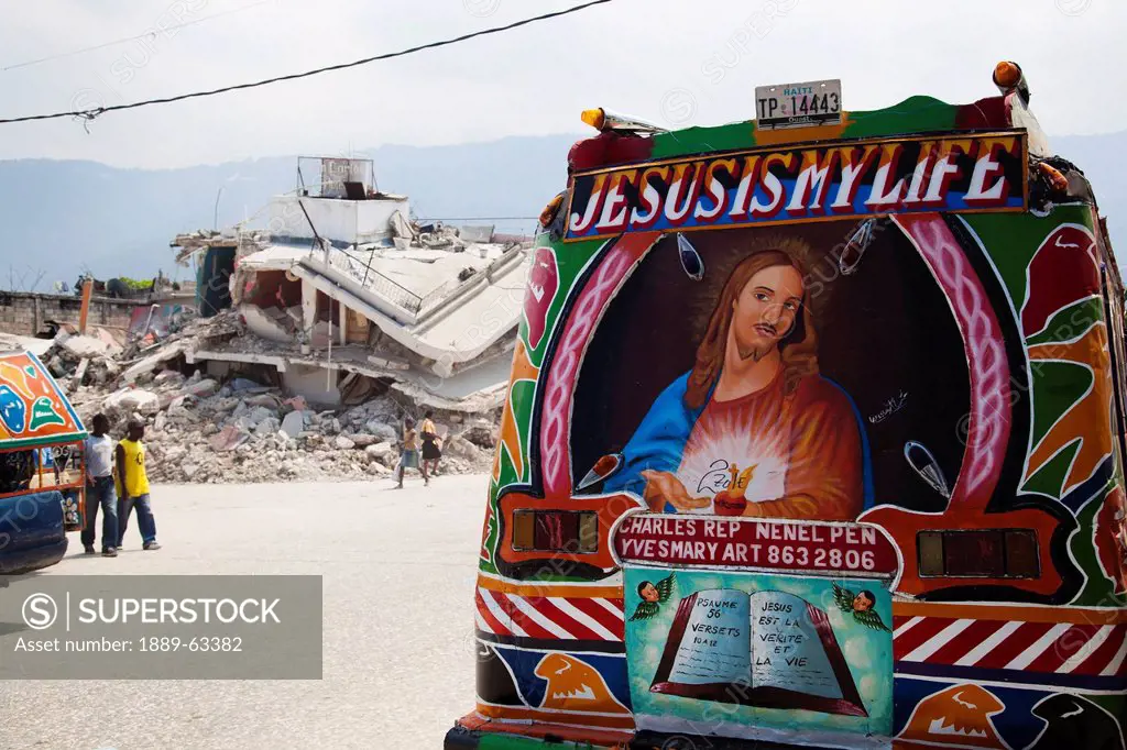 a painted vehicle saying ´jesus is my life´ with earthquake ruins behind it, port_au_prince, haiti