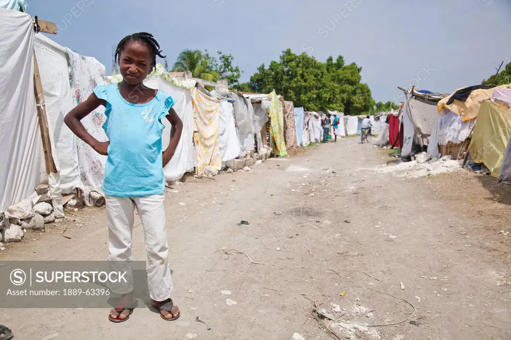 a girl stands by a row of tents made of bed sheets and plastic which are now home for many haitian families, port_au_prince, haiti