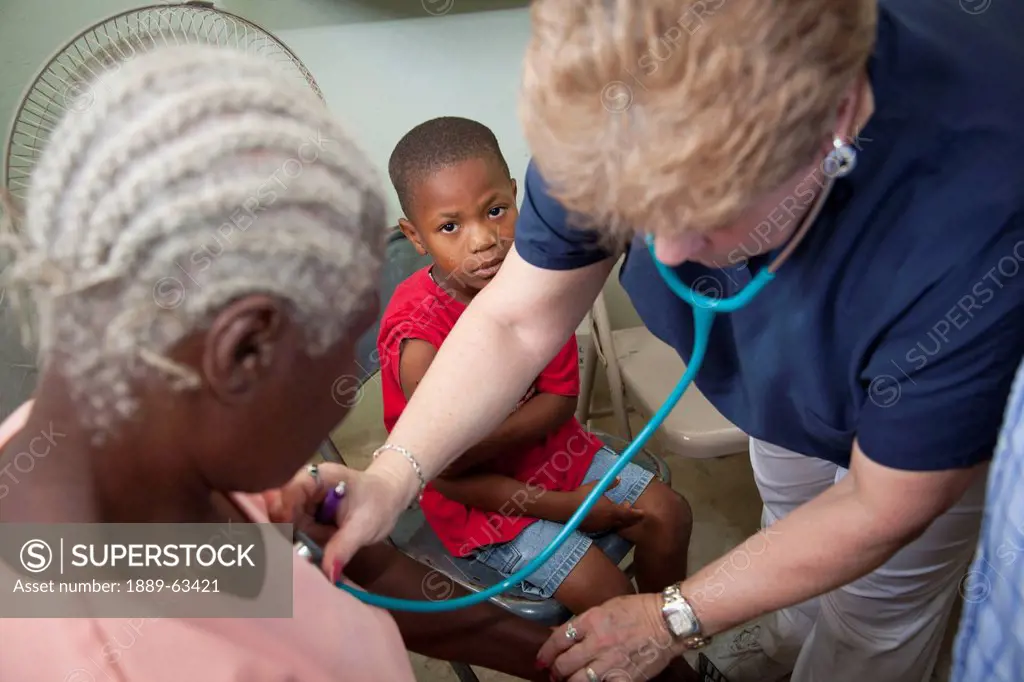 a nurse gives a check up to a woman while a boy looks on, grand saline, haiti