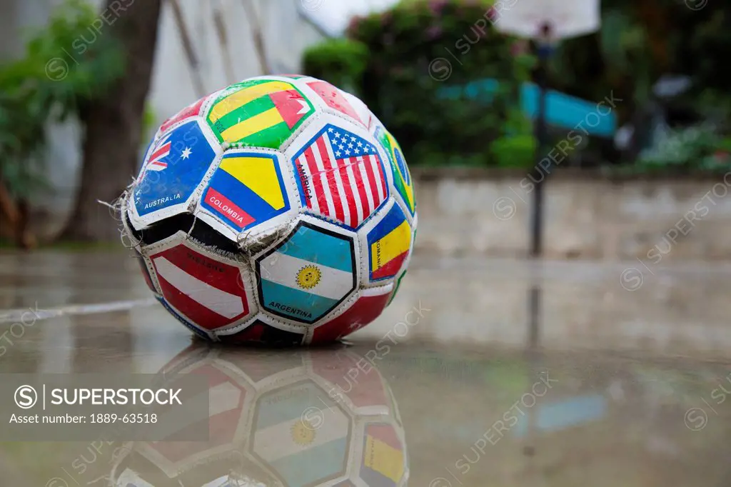 a soccer ball marked with various flags is ripped and sitting in water, port_au_prince, haiti