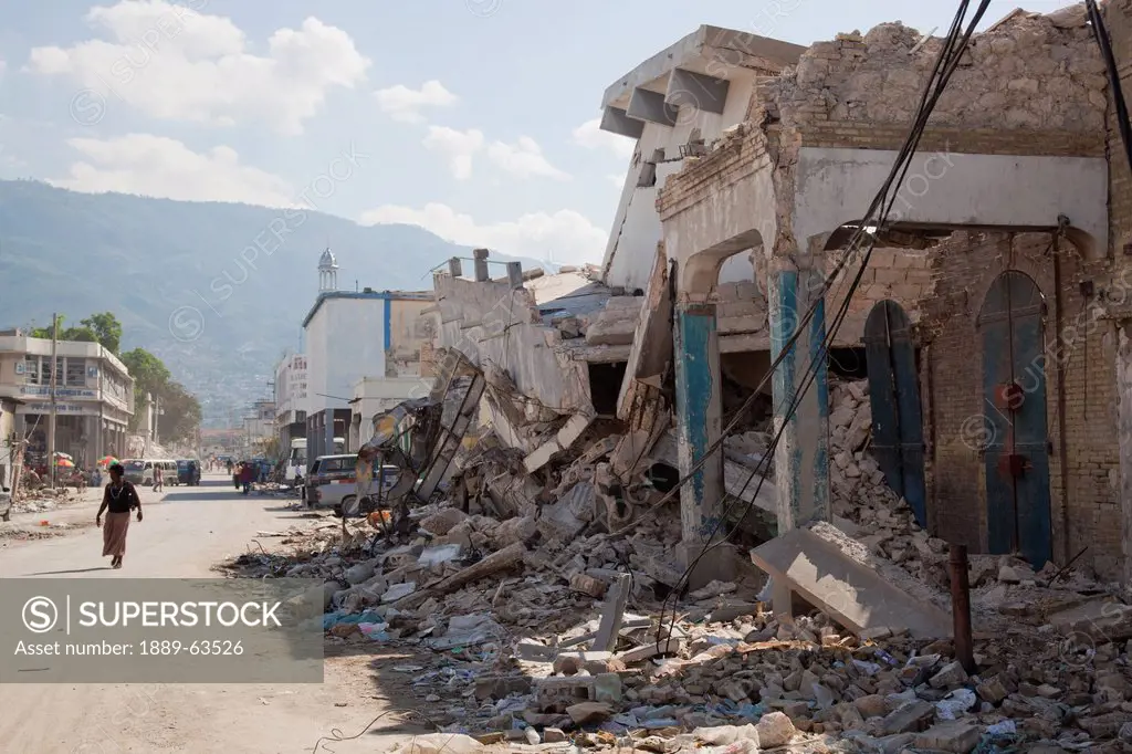 a person walks down the street beside collapsed buildings after the earthquake, port_au_prince, haiti