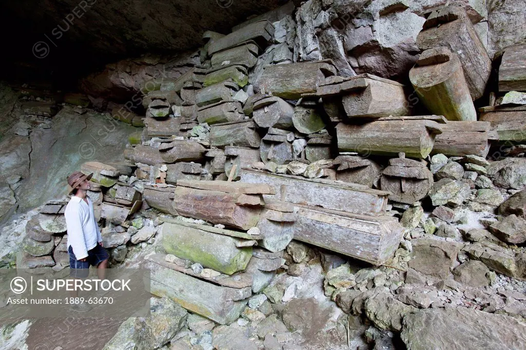 a male tourist looks at over 100 old wooden coffins that are stacked at the entrance to the lumiang burial cave near the mountain village of sagada, i...