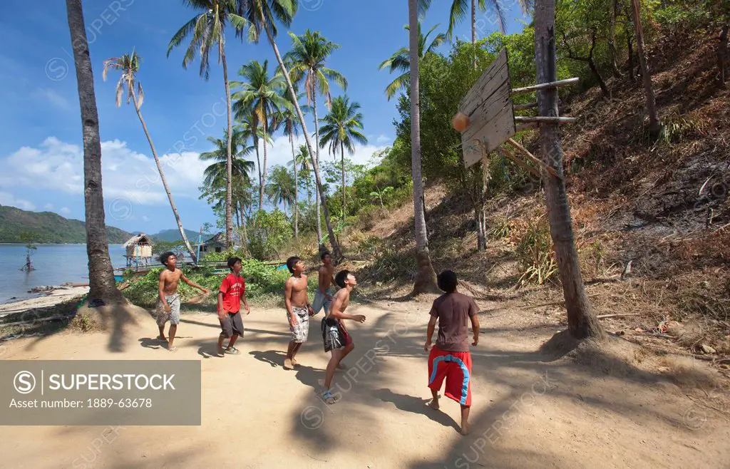 a group of teenage boys play basketball with the hoop attached to a coconut tree in the tiny fishing village of vigan near snake island and el nido, v...