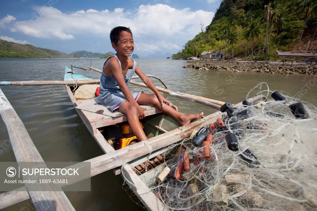 a young filipino boy smiles as he works on his family´s wooden bangka boat in the tiny fishing village of vigan near snake island and el nido, vigan, ...