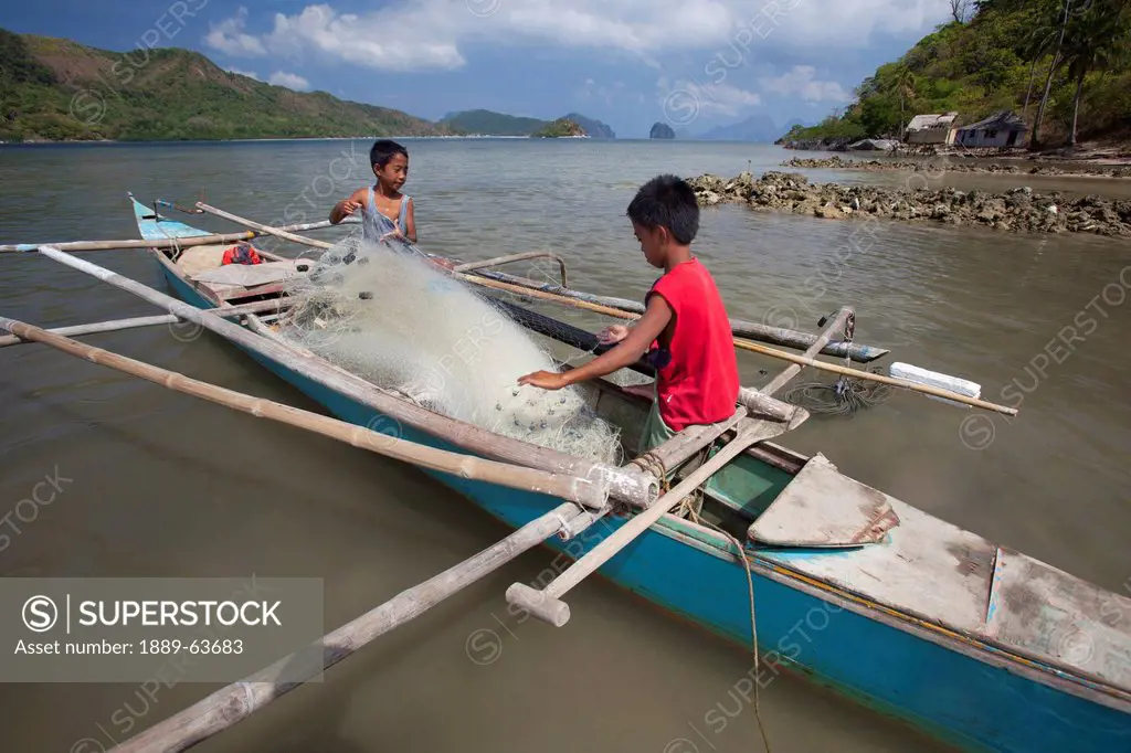 two young filipino boys work on their family´s wooden bangka boat in the tiny fishing village of vigan near snake island and el nido, vigan, bacuit ar...