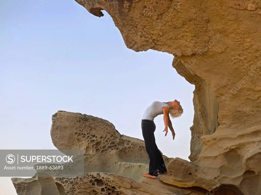 a woman bending backwards and looking up under a rock formation in parque natural del estrecho, tarifa, cadiz, andalusia, spain