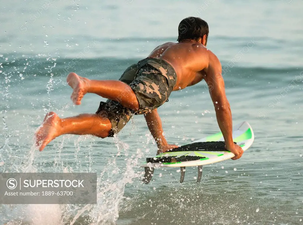 a man entering the water on a surf board off valdevaqueros beach, tarifa, cadiz, andalusia, spain