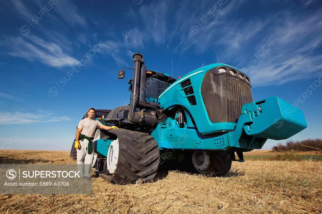 farmer posing by combine tractor, three hills, alberta, canada