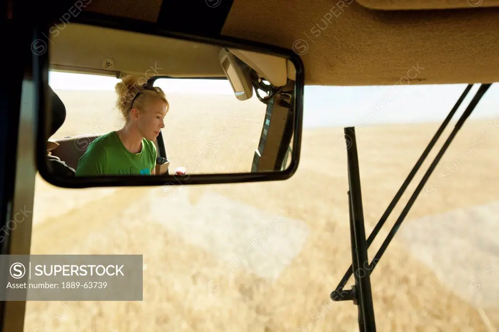 female farmer in combine seen in rear_view mirror, three hills, alberta, canada