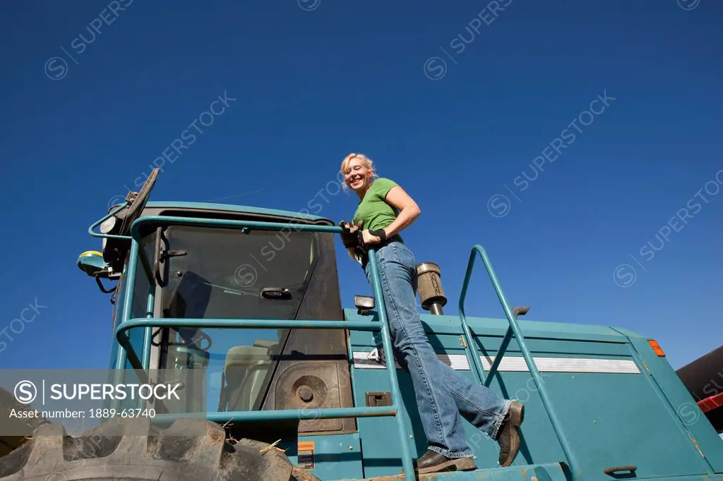 female farmer standing on combine tractor, three hills, alberta, canada