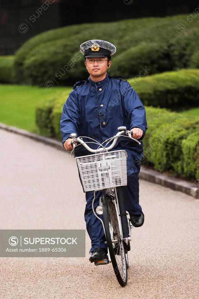 a guard riding a bicycle down a path at the imperial palace, tokyo, japan