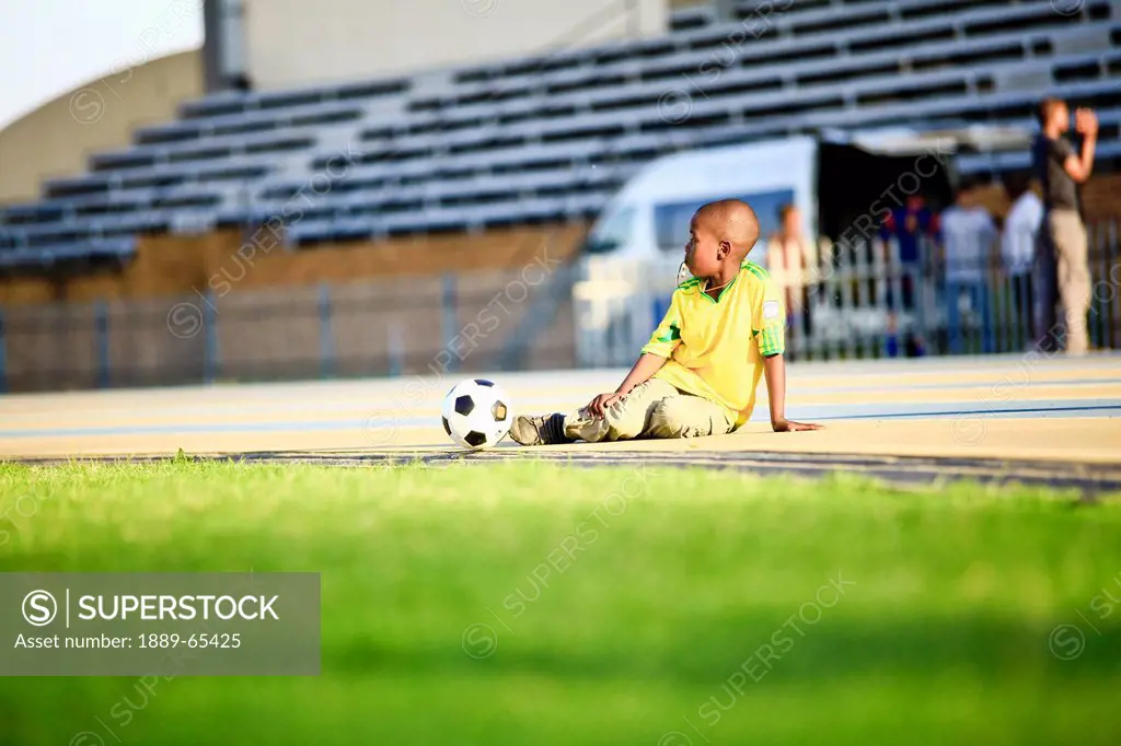 A Boy Sits On The Edge Of A Field With A Soccer Ball, Kampala Uganda Africa