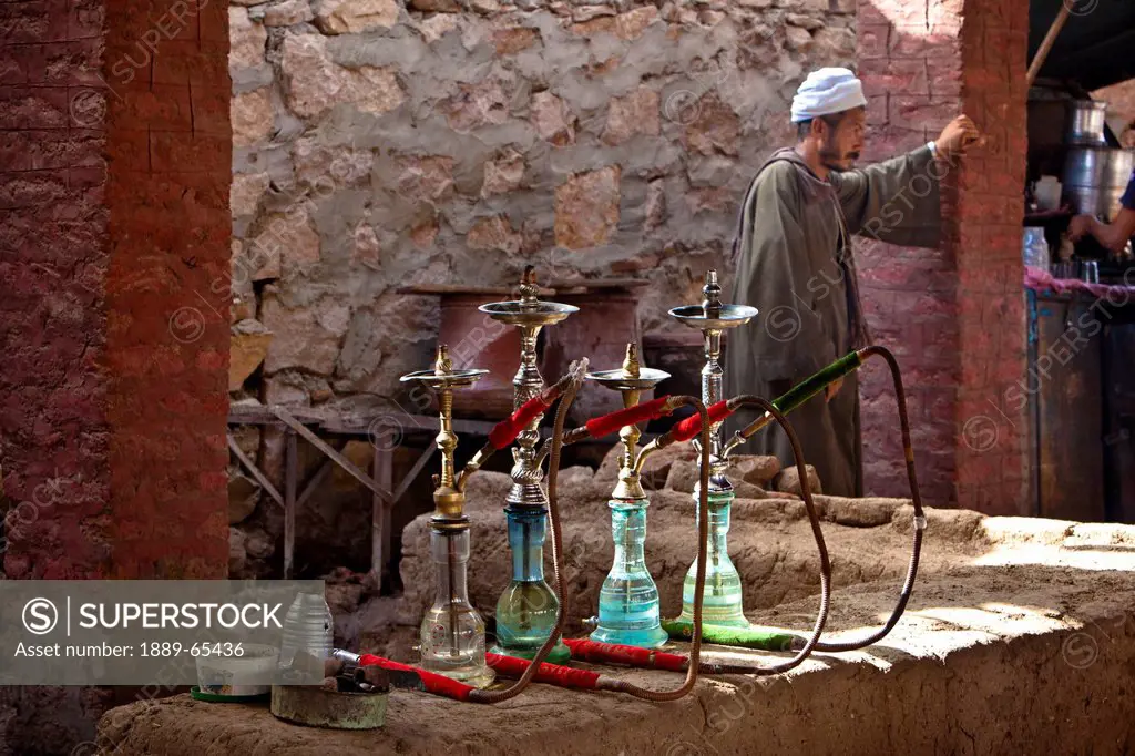 A Man Standing Outside A Tea House With Waterpipes Lined Up On A Ledge, Aswan Egypt