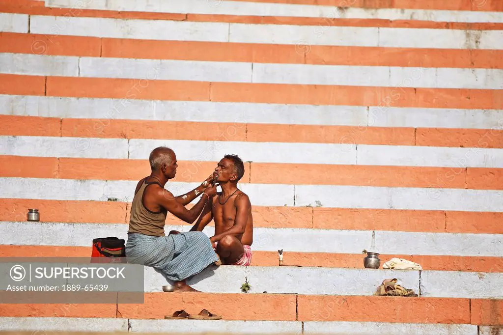 A Man Receiving A Morning Shave From A Barber On The Steps Of The River Ganges, Varanasi India