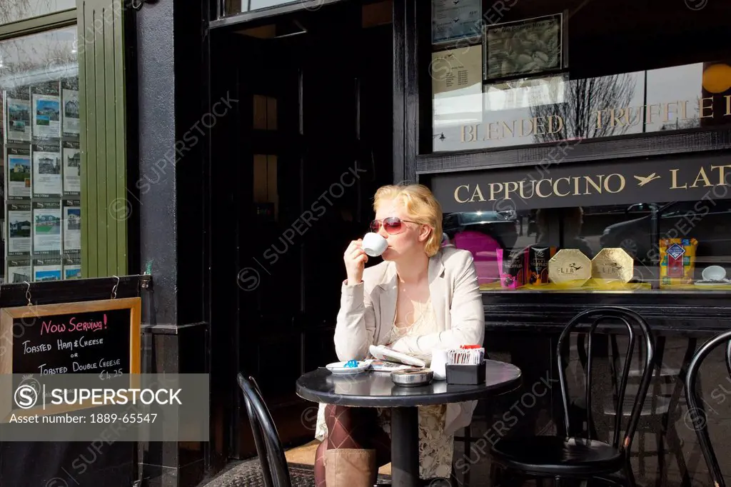 a young woman sits at a table at a cafe drinking coffee, killarney county kerry ireland