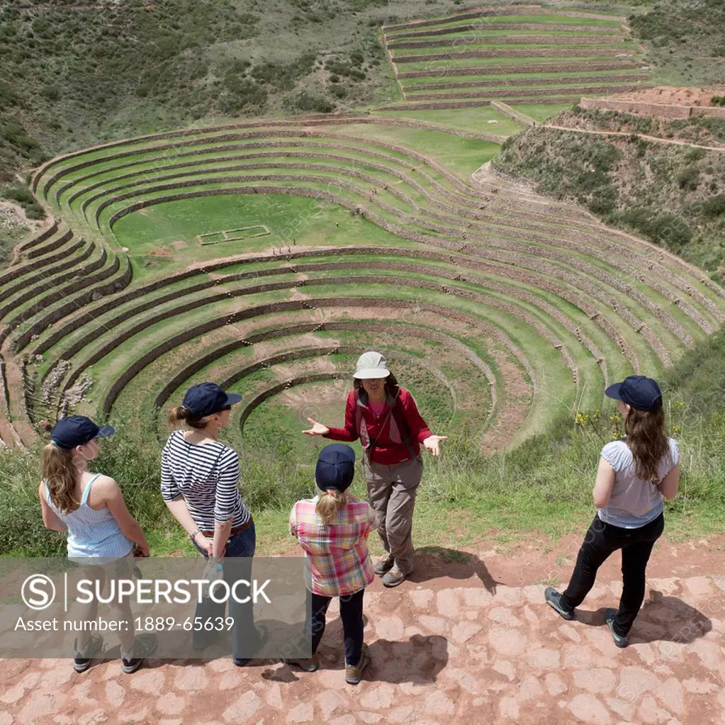 a group of young women overlook concentric ring terraces as part of the inca ruins, moray peru