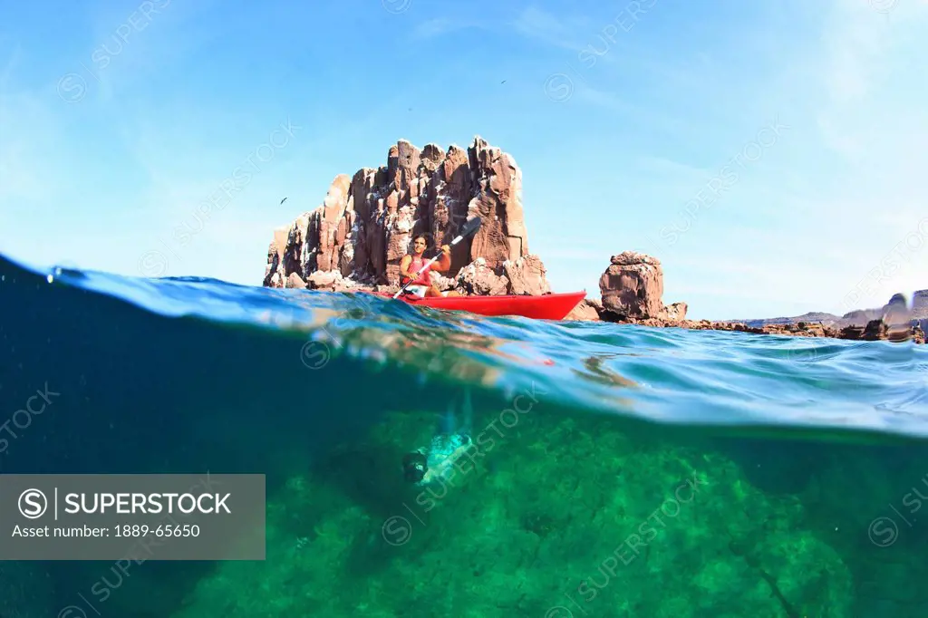 a person paddling on the water with a view of a large rock underwater at los islotes national marine park on espiritu santos island near la paz, baja ...