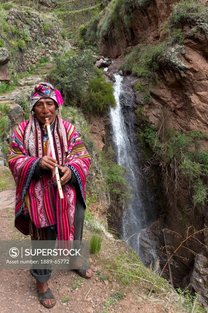 musician playing flute by waterfall at archaeological park of pisac, pisac peru