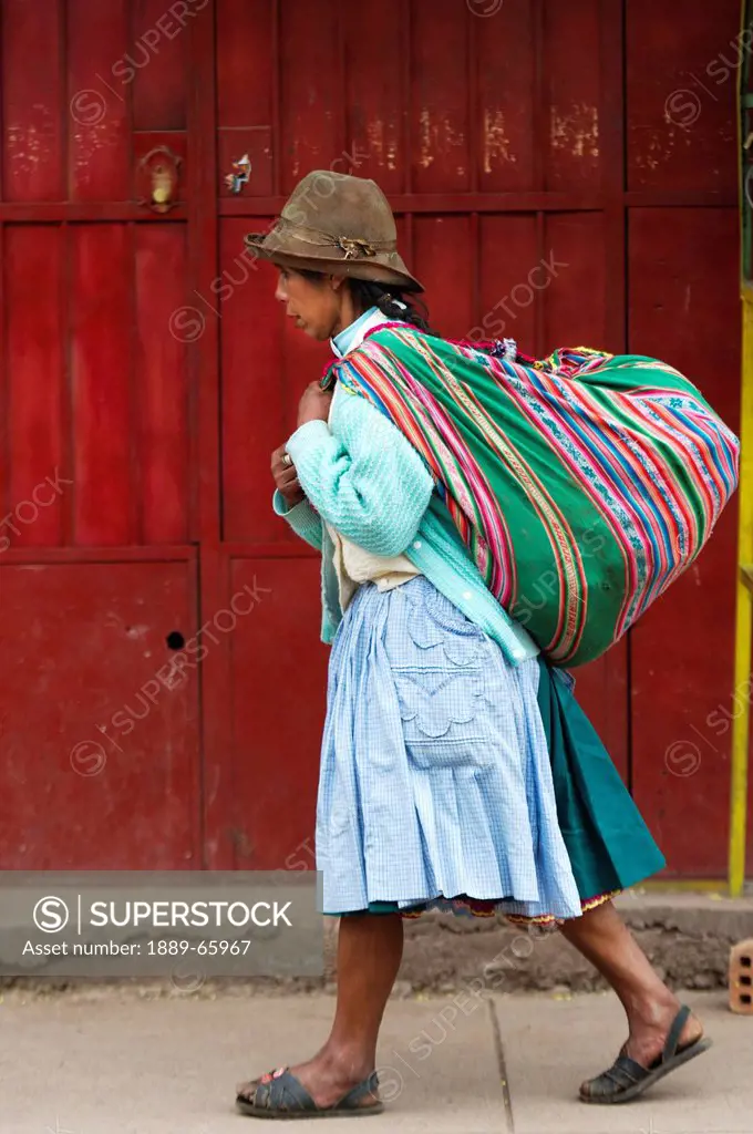 A Woman Walks On A Sidewalk Carrying A Bundle Over Her Shoulder, Cusco Peru