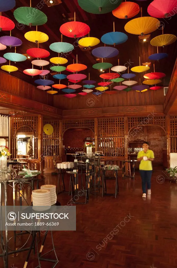 a server walks under umbrellas hanging from the ceiling at the restaurant in amari rincome hotel, chiang mai thailand