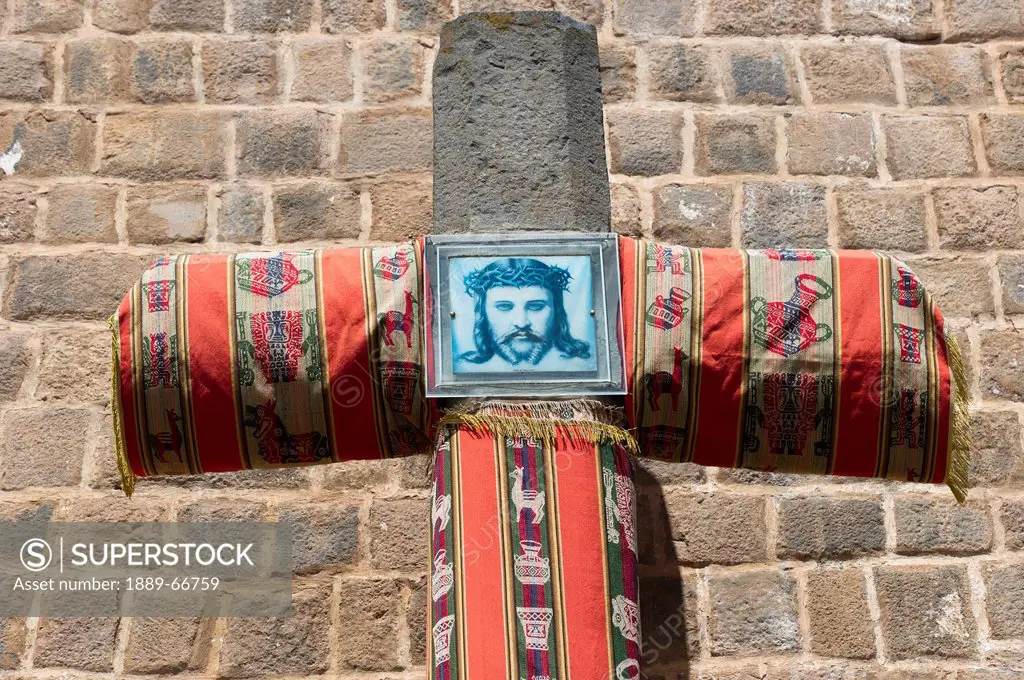 A Picture Of Jesus Christ On A Fabric Covered Cross Against A Brick Wall, Cusco Peru